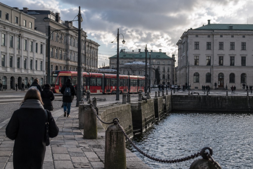 Red tram passing through a Gothenburg street with stone buildings under a grey sky