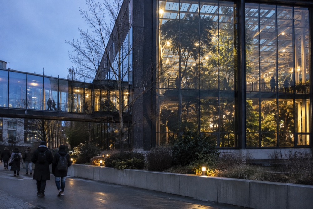 Visitors walking through a glass-roofed rainforest hall inside a science centre with tall trees and a walkway