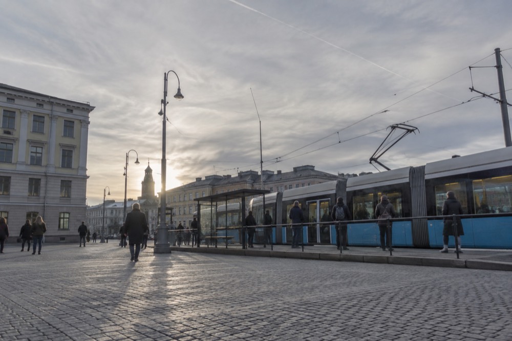 A blue Gothenburg tram at a street stop with passengers waiting on the platform