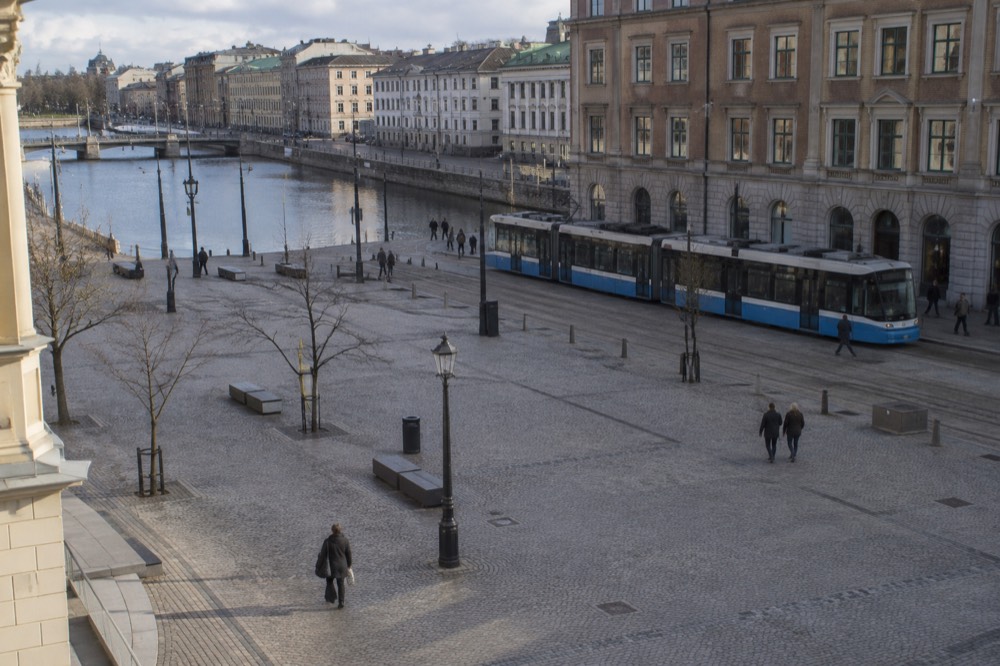 A blue Gothenburg tram passing a brick building on a city street