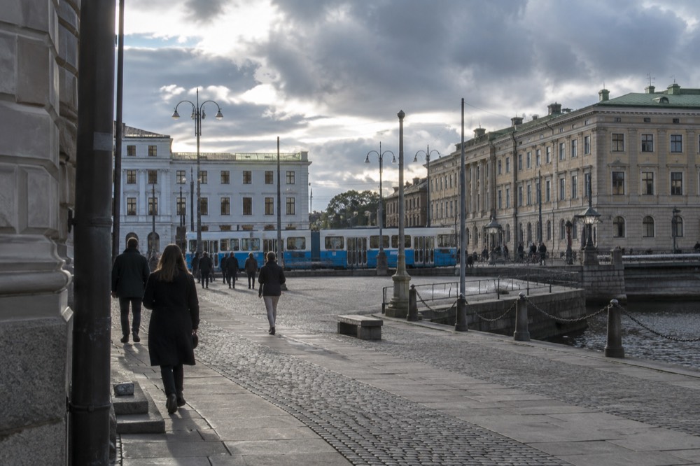 A blue Gothenburg tram moving along a street with granite buildings behind it