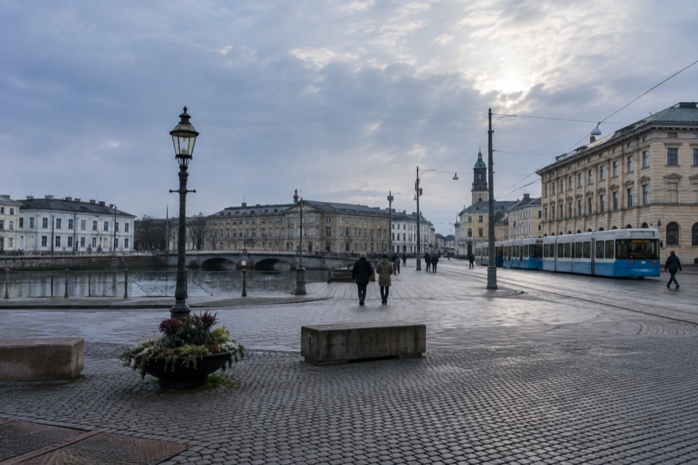 Trams and stone buildings along a canal in central Gothenburg under a grey sky