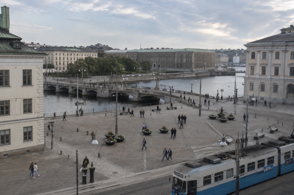 A tram stop sign in central Gothenburg with passengers waiting on a granite street