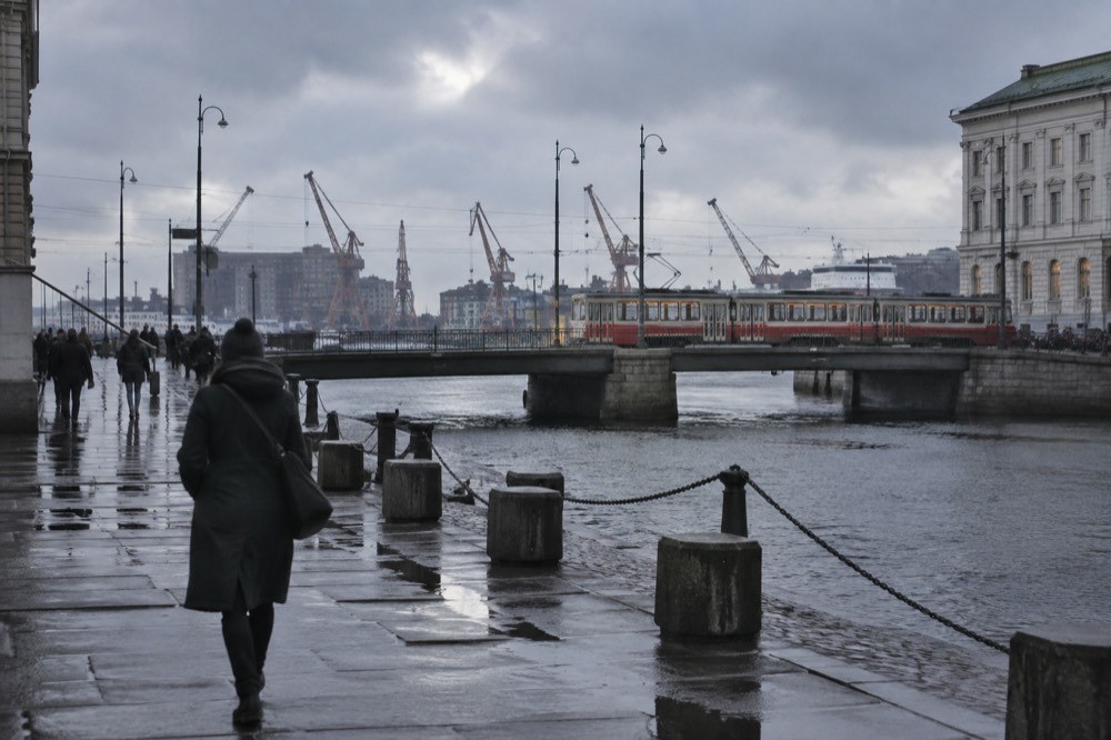Rain clouds over Gothenburg harbour with shipyard cranes and a red tram crossing a bridge in wet conditions