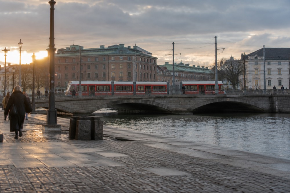 Red Gothenburg trams crossing a stone bridge over the canal, with brick buildings behind them