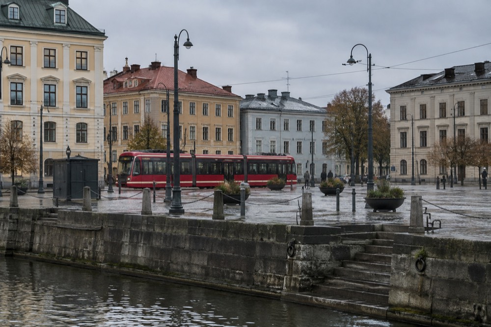 Red tram passing painted wooden houses on a Gothenburg street under a grey Nordic sky