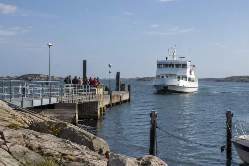 A white Västtrafik archipelago ferry approaching a small island jetty with waiting passengers