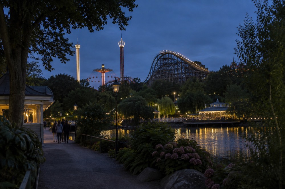 Wooden roller coaster structure and lit amusement park rides against a dark evening sky