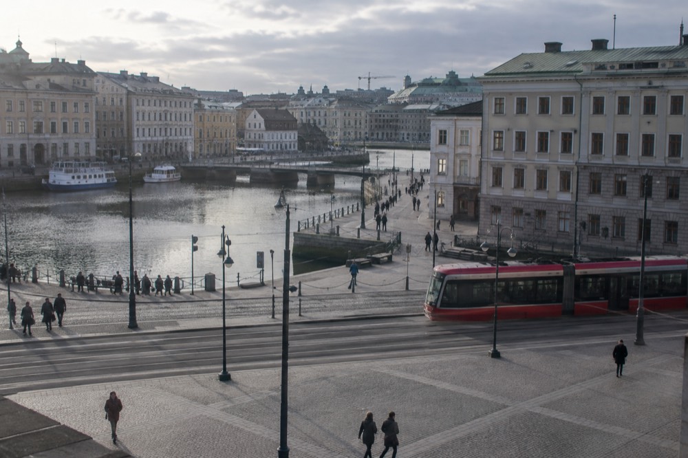 Red tram passing through a Gothenburg street with stone buildings under a grey sky