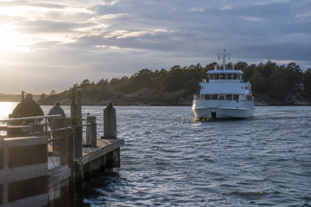 A white passenger ferry approaching a wooden jetty on a green island in the Gothenburg archipelago