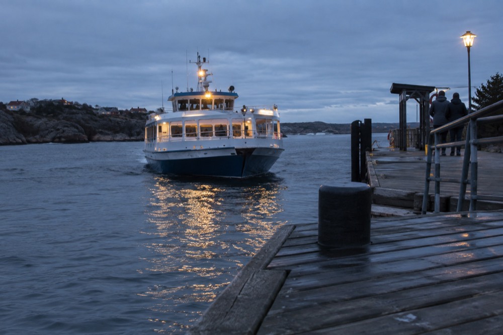 A small ferry approaching a wooden pier on a rocky island in the Gothenburg archipelago