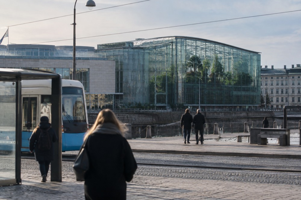 A large glass science centre building with a rainforest canopy visible inside, seen from a tram stop on a wide avenue