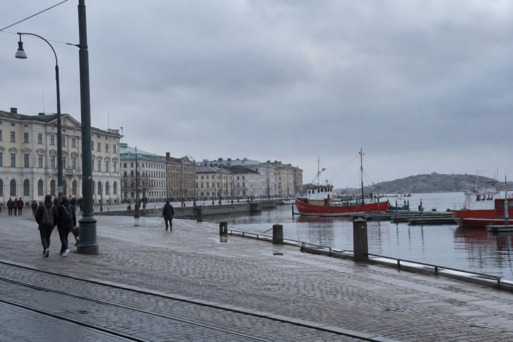 Red wooden boats moored in a Gothenburg harbour with granite islands behind them under a grey sky
