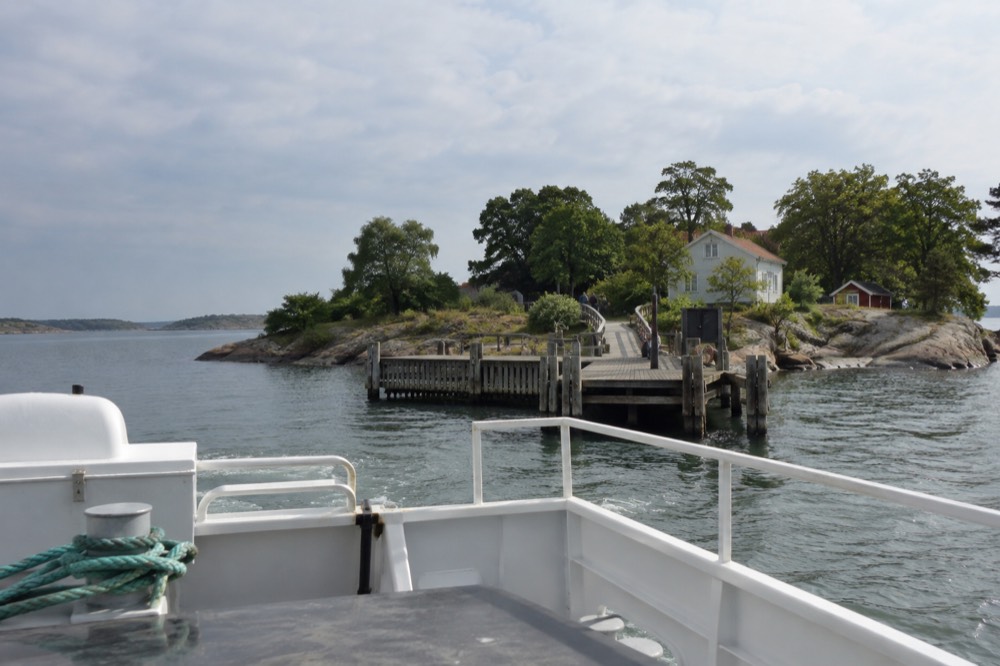 A white passenger ferry approaching a wooden jetty on a green island in the Gothenburg southern archipelago