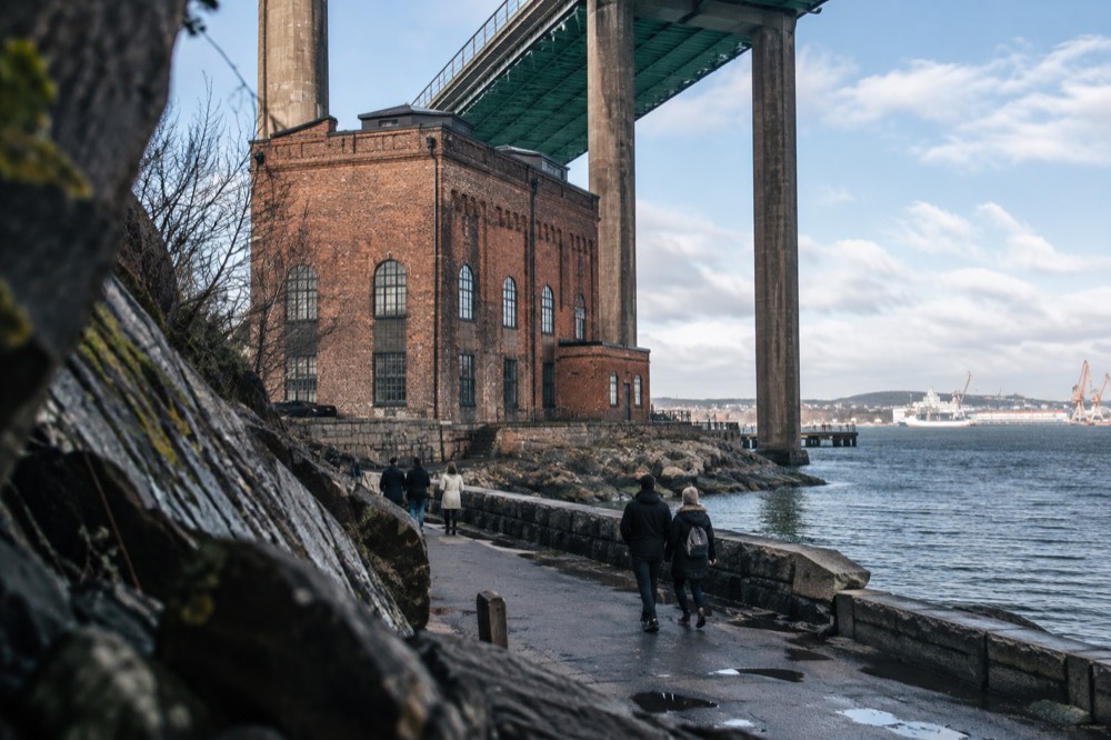 Visitors walking the riverside path beneath the Älvsborg Bridge on a bright afternoon