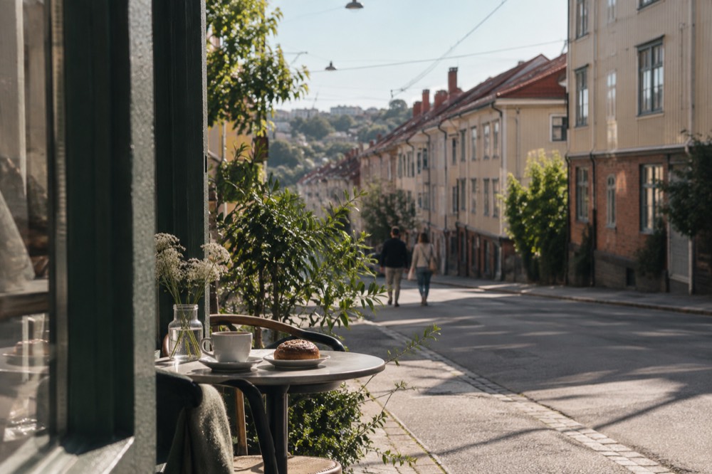 A cafe table with coffee and a pastry beside a shop window in Majorna