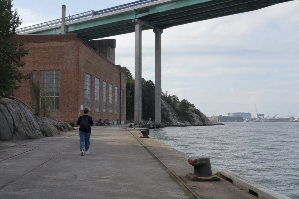 A visitor walking the concrete quay beneath the Älvsborg Bridge approach ramps