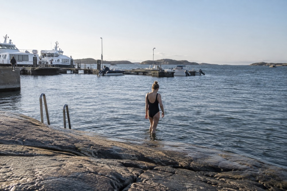 A swimmer stepping into the sea from a smooth granite rock under a clear sky