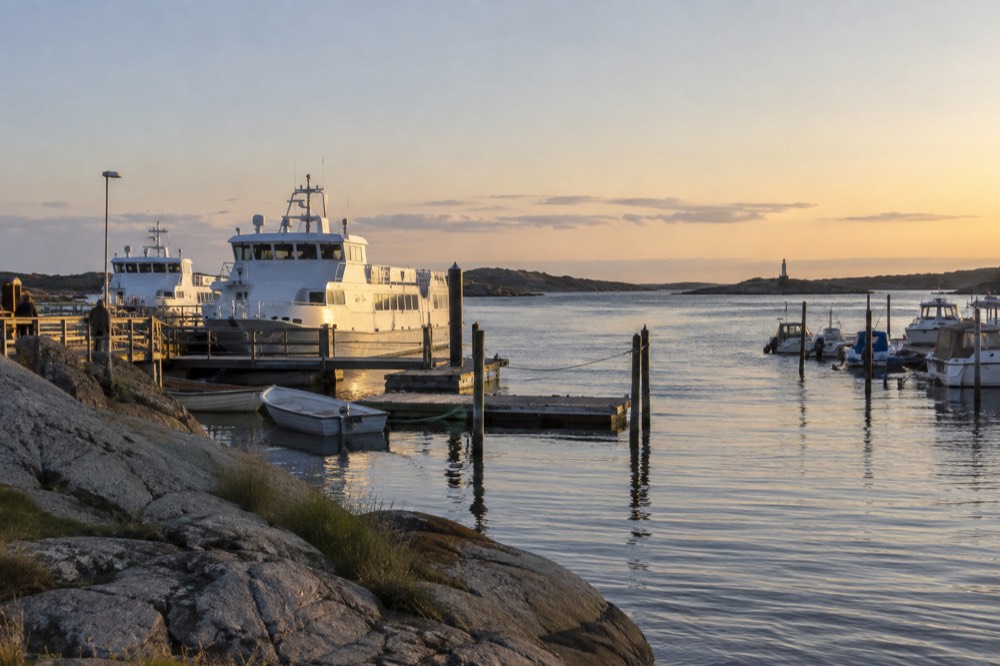 Evening light over a calm harbour with small boats and a distant lighthouse