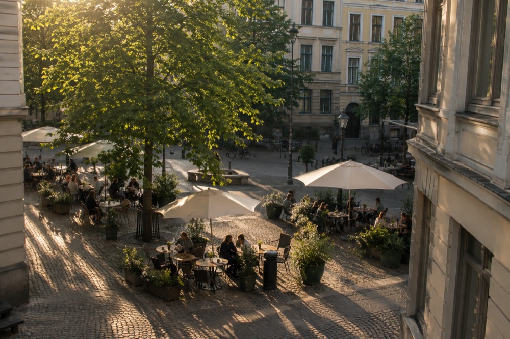 People sitting at outdoor café tables on a small square surrounded by stone buildings