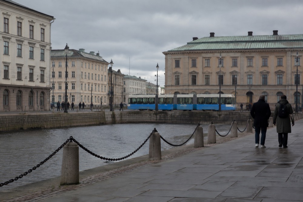 A blue Gothenburg tram passing stone buildings on a street near the old town
