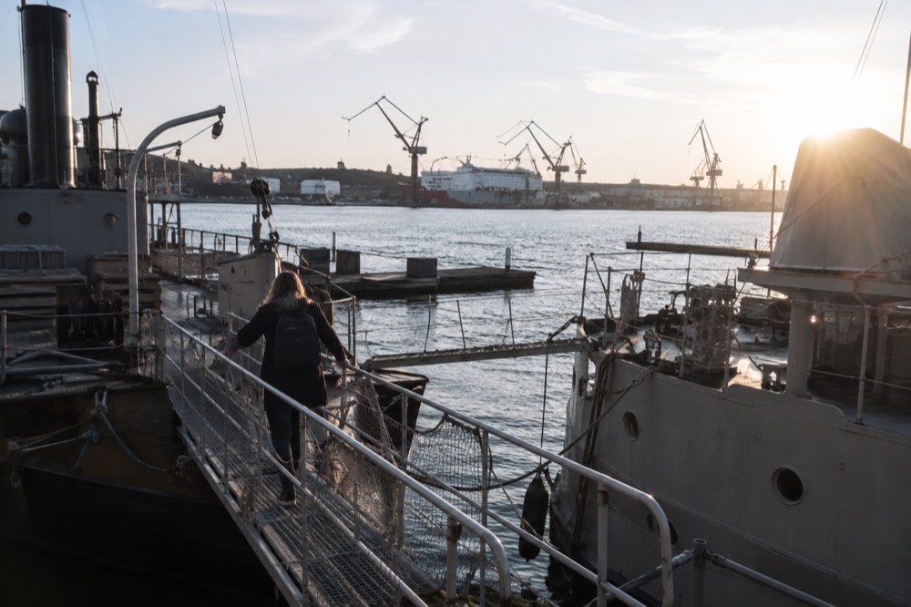 A visitor climbing a metal gangway between two moored museum ships