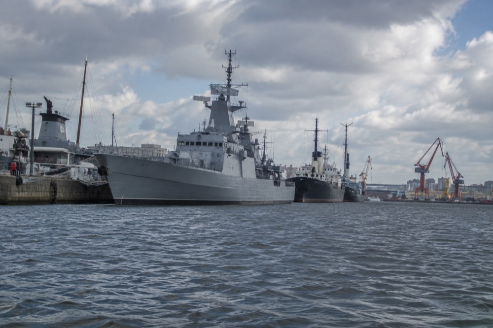 A grey naval destroyer moored at a city quay seen from the water