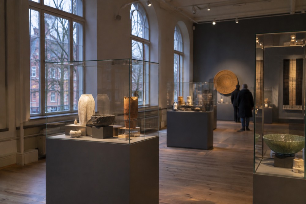 A gallery interior with glass display cases showing craft objects under focused lighting