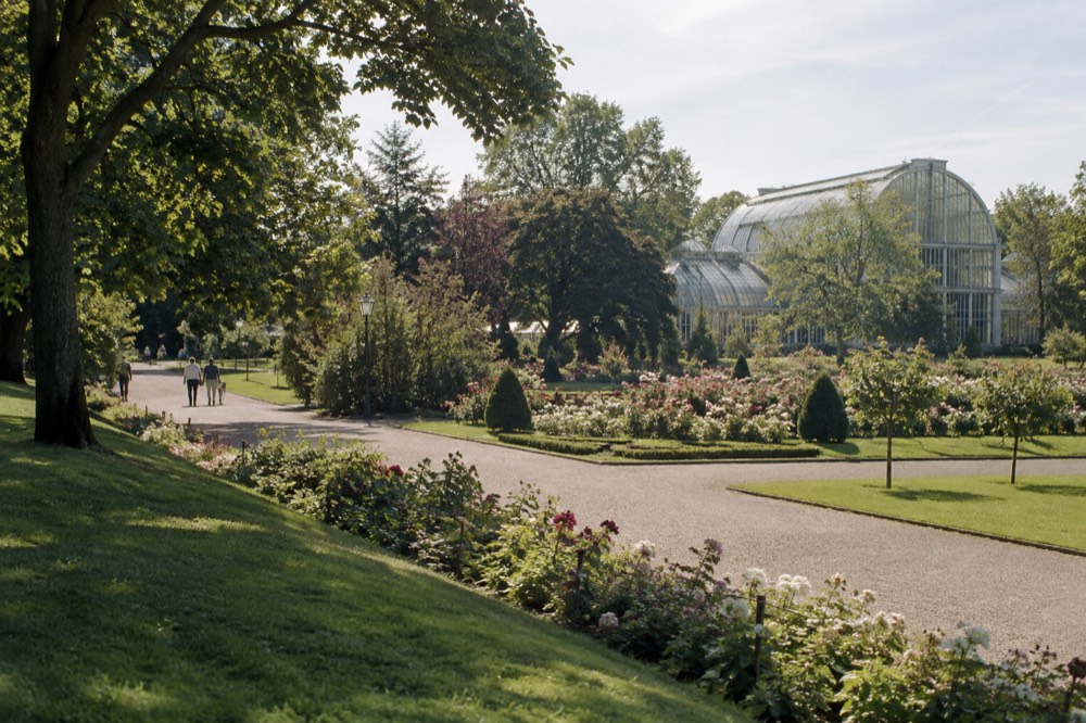 A green park path in central Gothenburg with flowerbeds and mature trees on a bright day