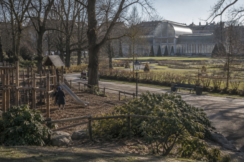 A wooden playground with climbing frames and slides under tall trees in a city park