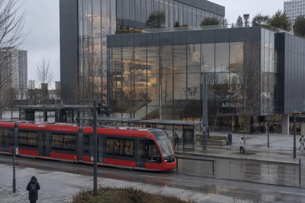A red Gothenburg tram passing a stop in front of a modern building