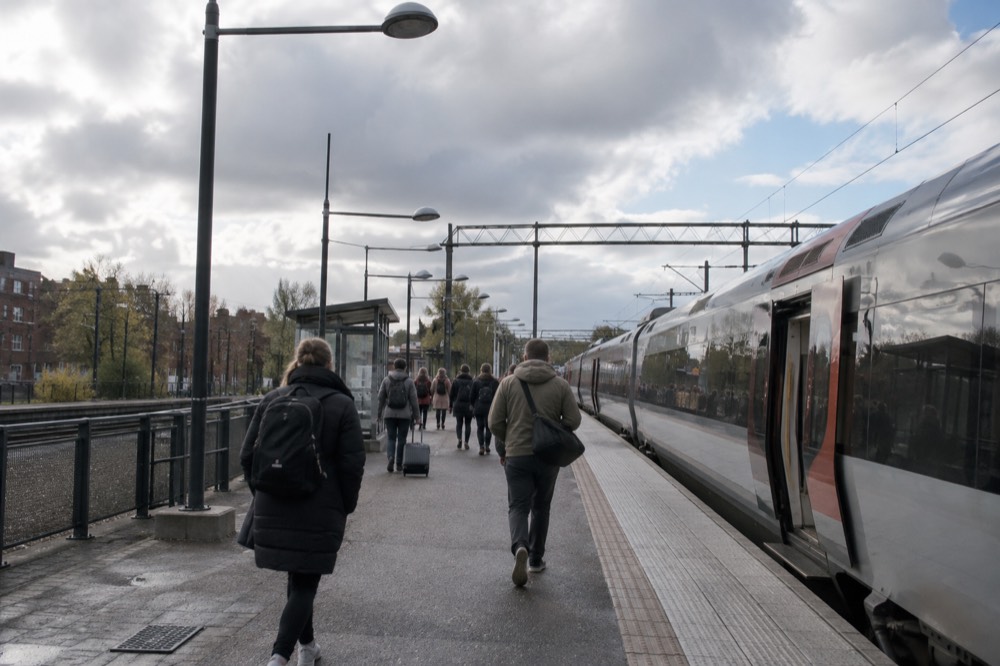Passengers walking along a station platform toward a regional train on an overcast day