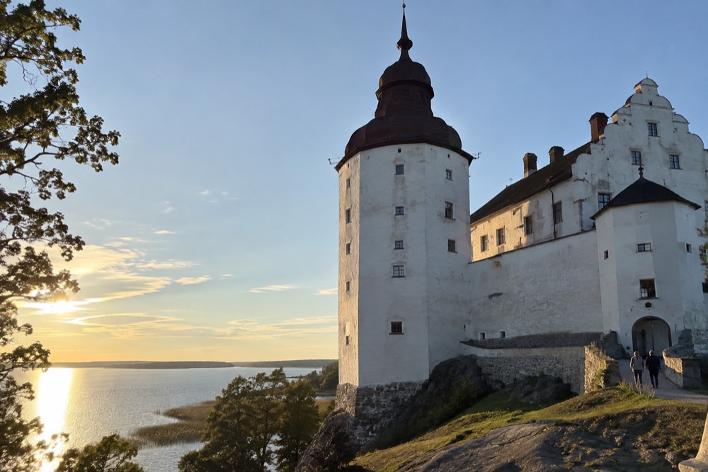 A castle tower seen from below against a blue sky with lake water glittering behind
