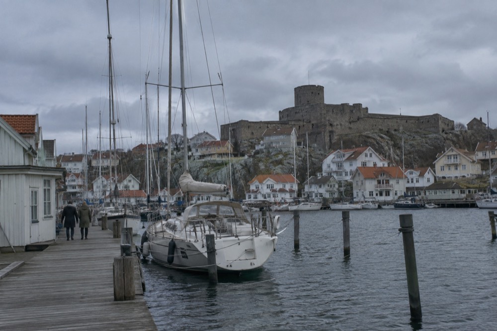 A small island town with a stone fortress on a rocky hill above wooden houses and a harbour