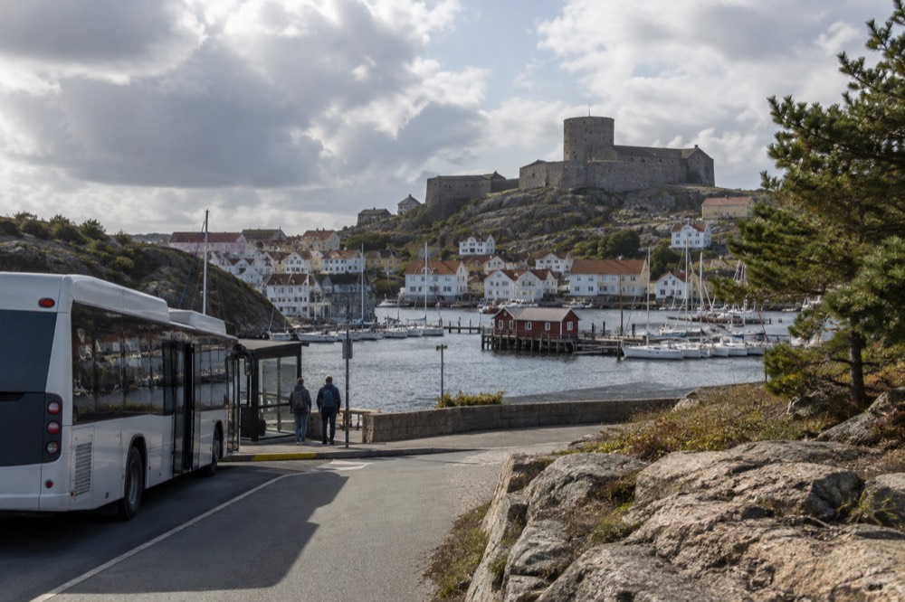 A regional bus at a small coastal stop with granite rocks and pine trees