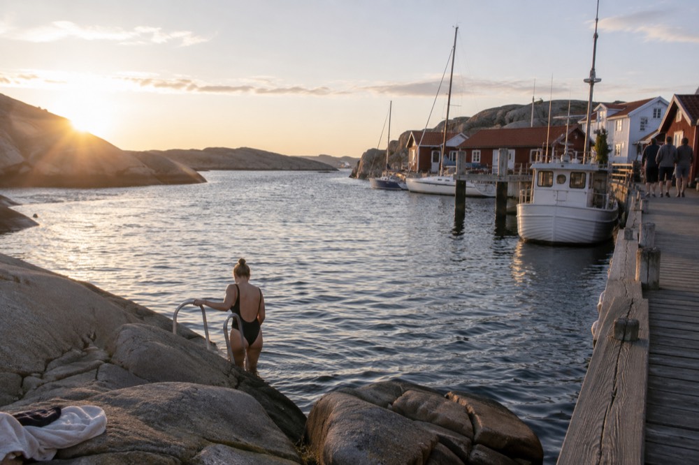 A swimmer stepping from bare granite rock into clear sea