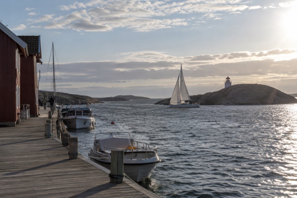 A sailing boat passing a granite island with a small lighthouse