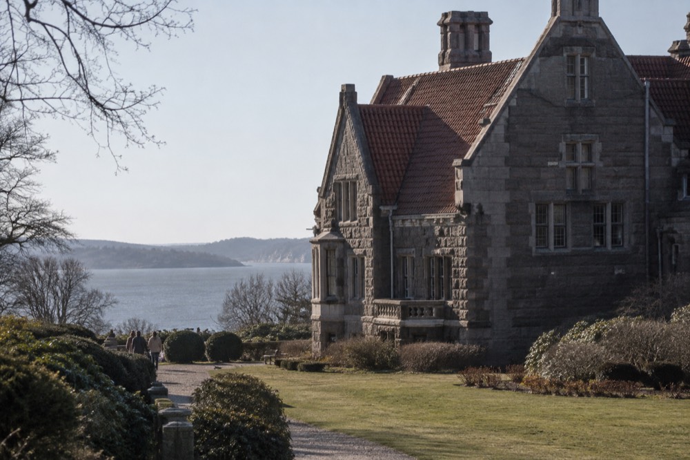A steep gabled roof of dark red tile above stone walls, seen from a garden path