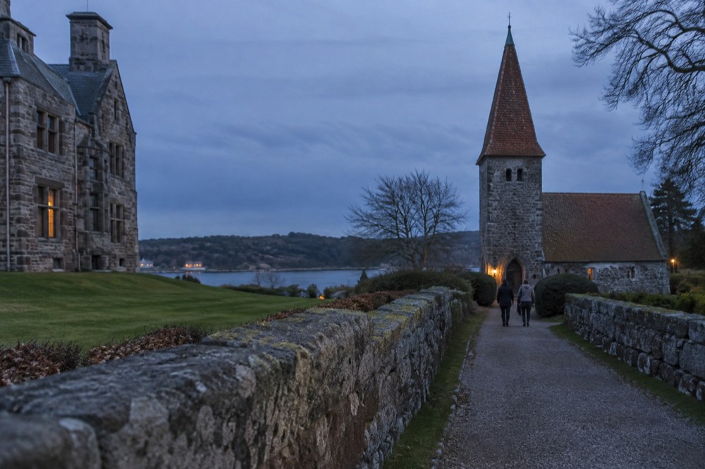A gravel path leading between low stone walls toward a church with a tiled spire