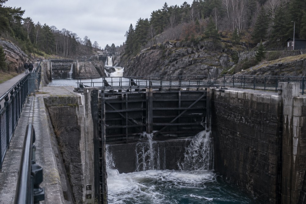 A flight of canal locks descending through a Swedish town, with water pouring between stone walls and a walkway alongside