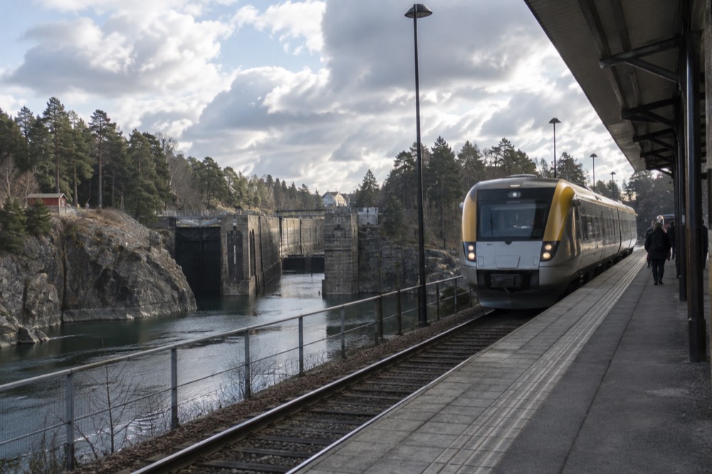 A Swedish regional train at a small station platform beside a river valley