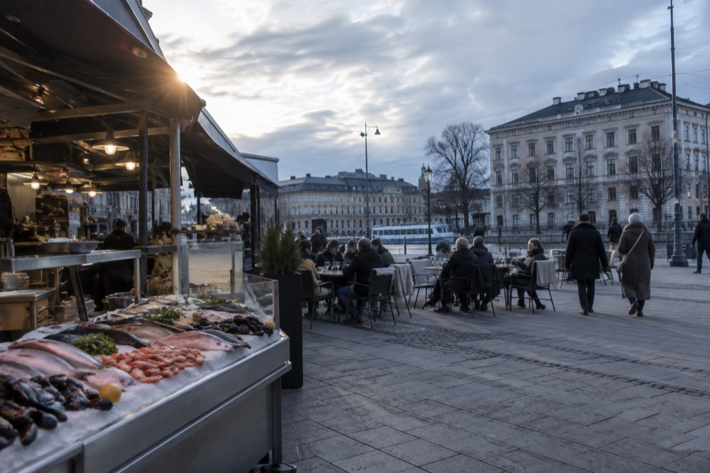 A busy Gothenburg food hall counter with fresh seafood on ice and diners at small tables