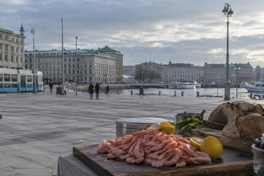 Cold peeled shrimp piled on a wooden board beside lemon and bread at a Gothenburg counter