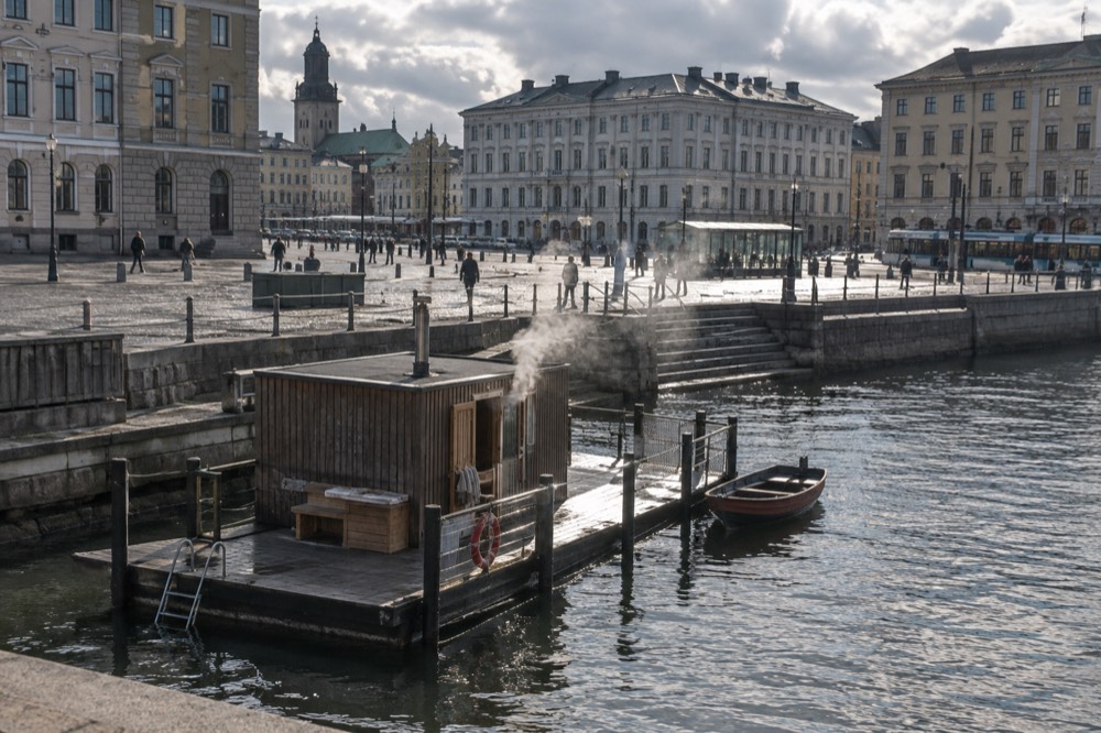 A sauna boat at a wooden pier with steam rising from its hot room door