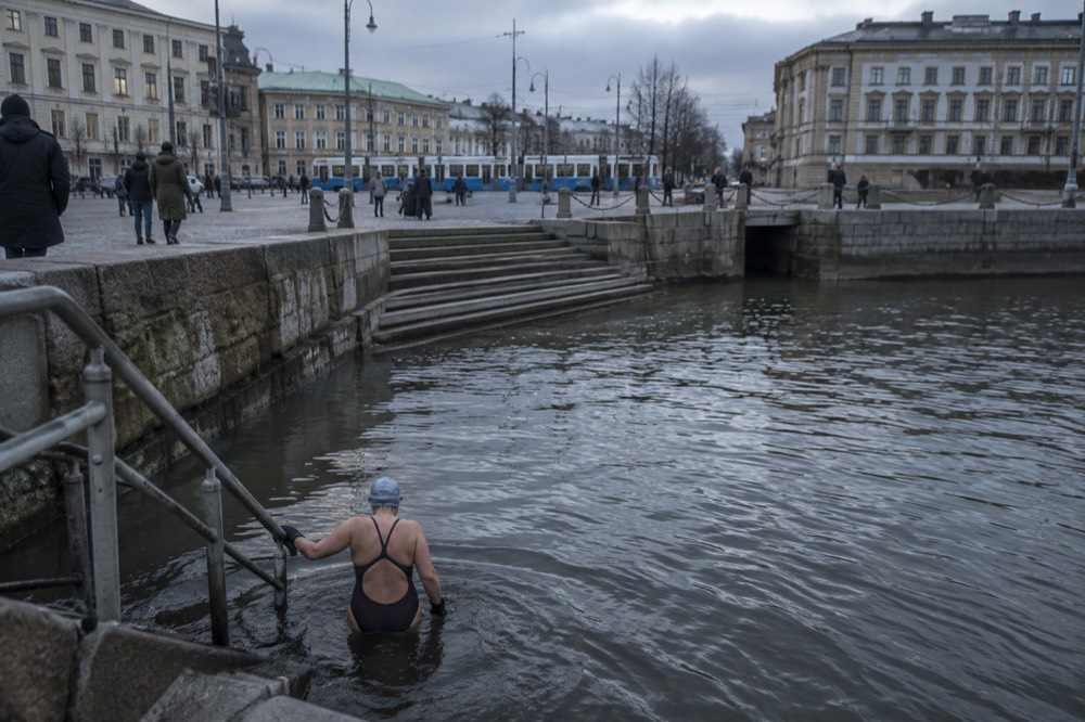 A swimmer in a cap and neoprene gloves entering grey winter water from granite rocks