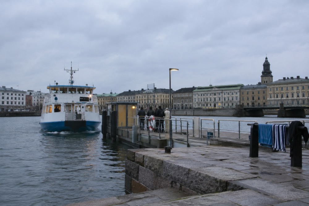 A ferry approaching a small island jetty with swimmers' towels drying on a railing