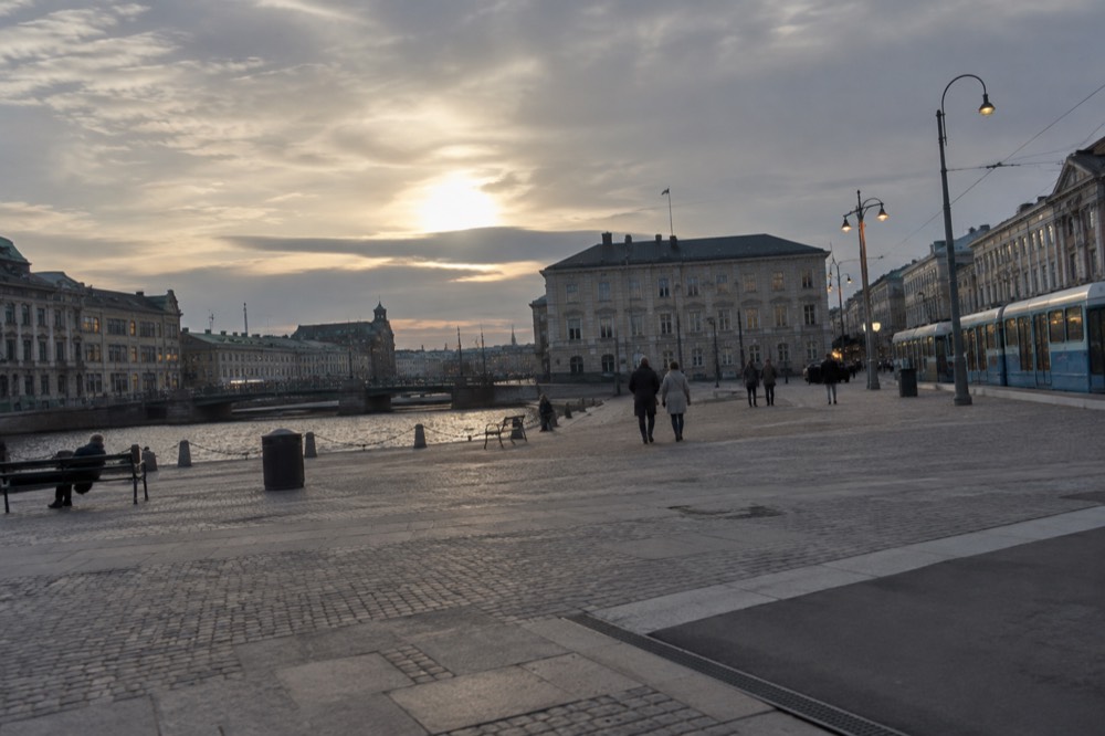 A northern city street lit by warm lamps under a dark blue early evening sky
