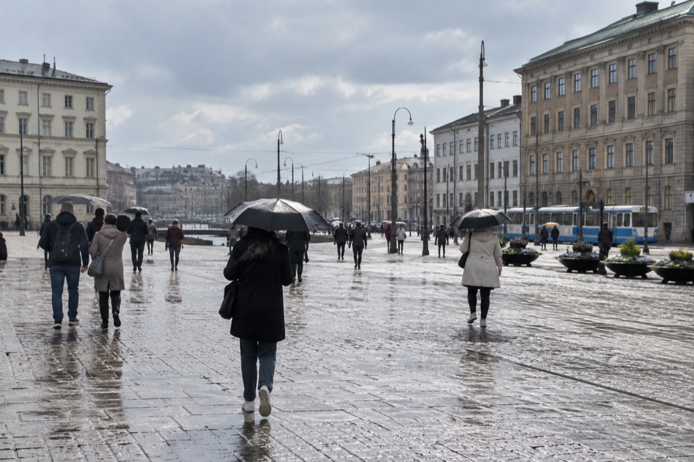 Visitors under umbrellas walking past brick buildings in central Gothenburg