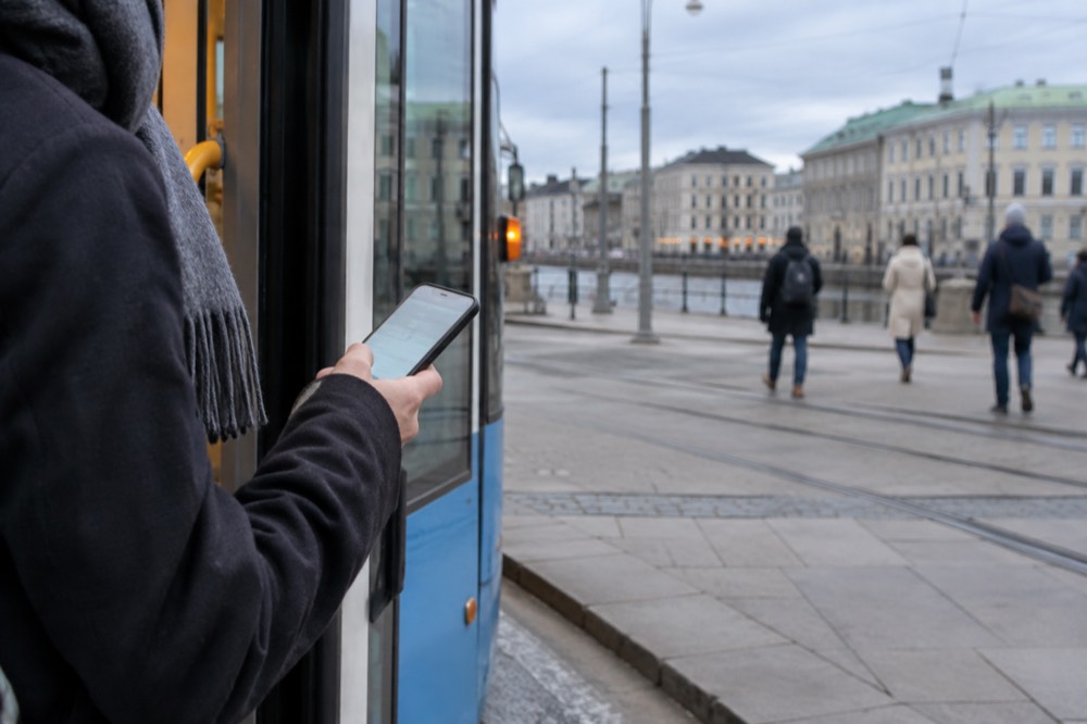 A hand holding a phone showing a ticket app beside a tram door in Gothenburg
