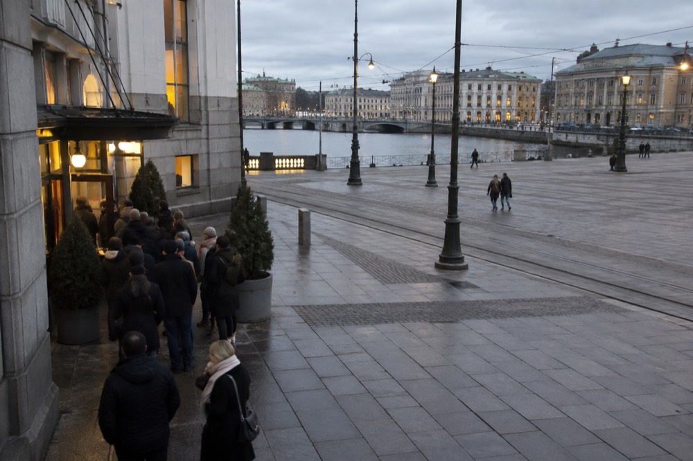 Audience members queuing outside a cinema entrance in evening light